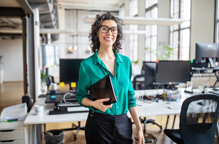 woman clutching tablet in office smiling at camera