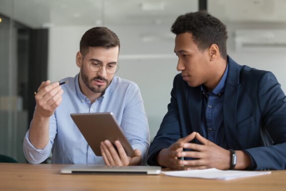 two men at desk looking at tablet