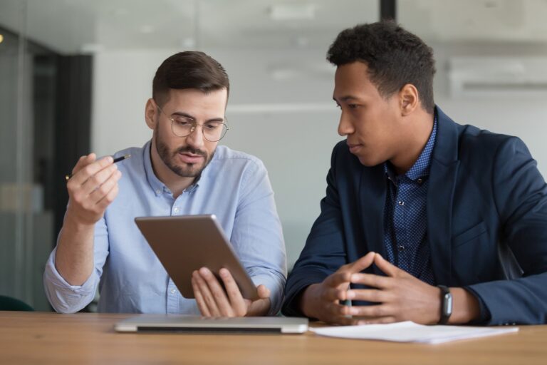 two men at desk looking at tablet