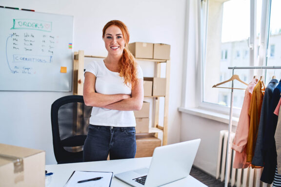 woman with folded arms smiling at desk with whiteboard in background