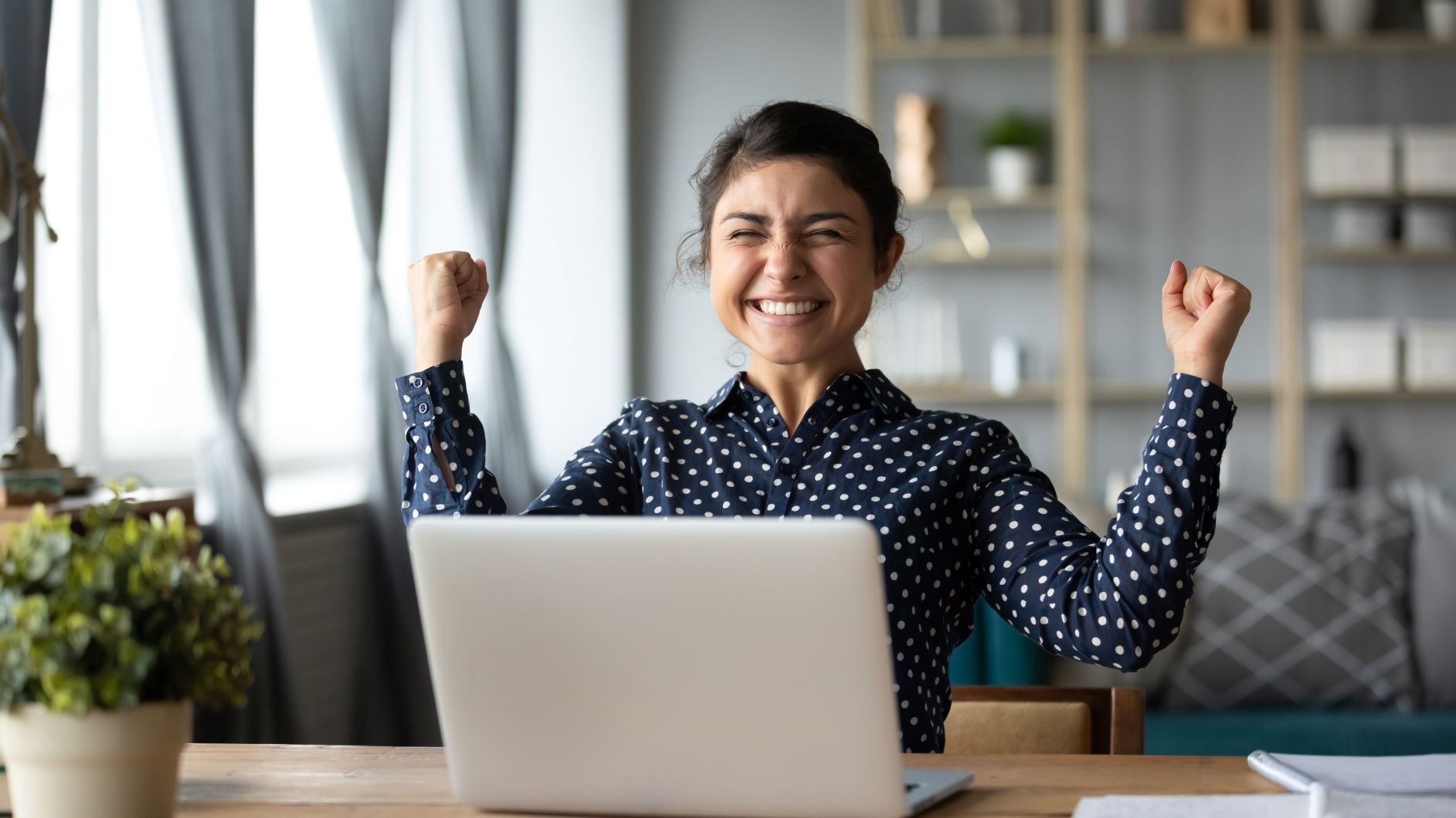 Woman sitting at laptop clenching fists in celebration