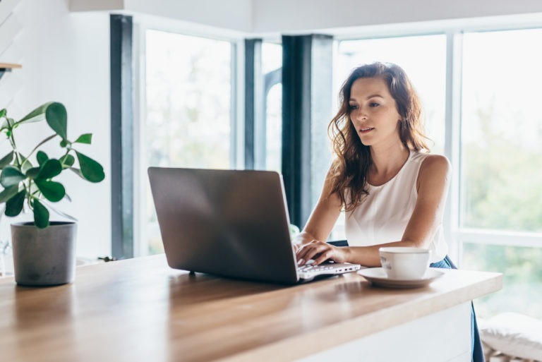 Woman with coffee next to her working on laptop