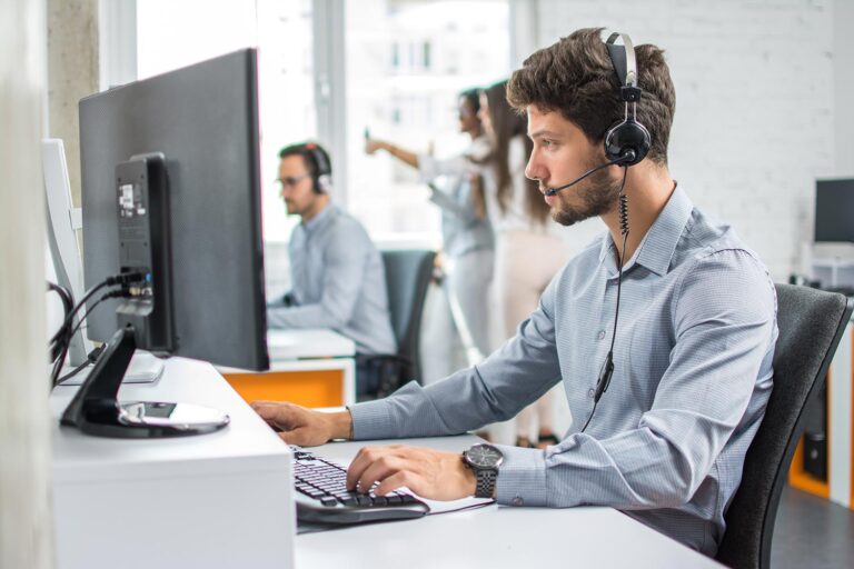 man wearing a headset looking at a computer with people talking behind him