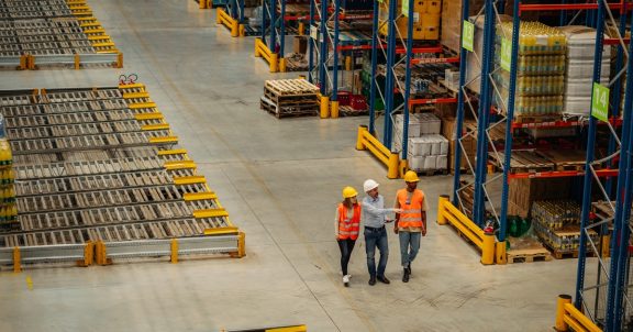 Businessman with a digital tablet showing and talking with two workers in distribution warehouse
