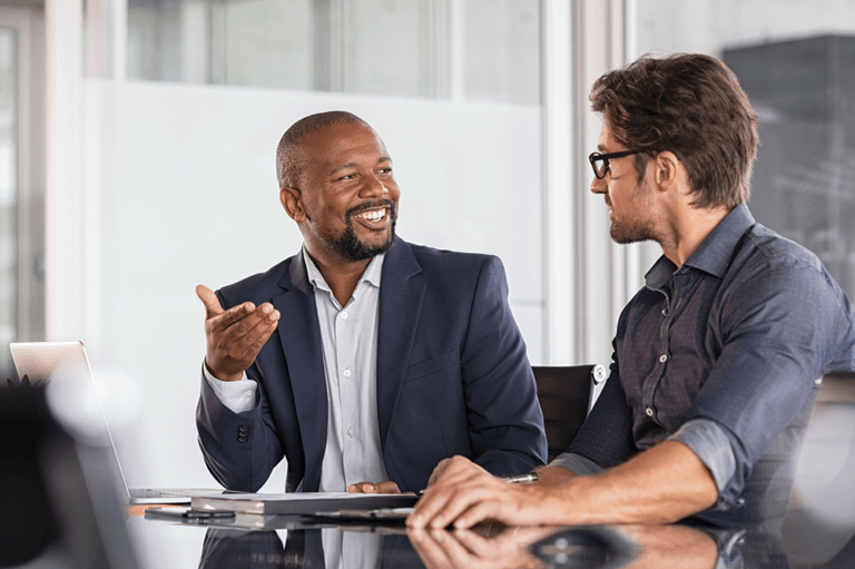 2 people at a table talking to each other with a notebook sitting on the table
