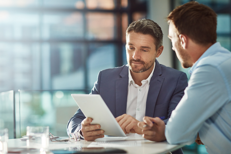 2 men sitting at a table looking at a tablet