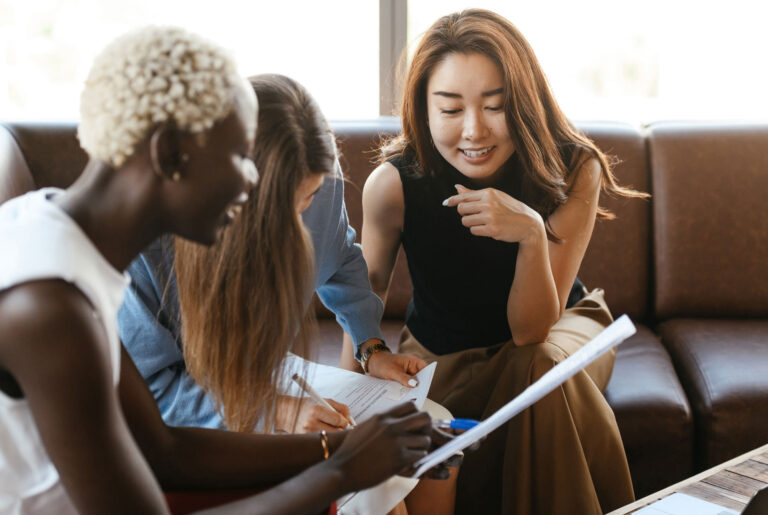 3 women sitting on a couch with one pointing to a piece of paper and one taking notes