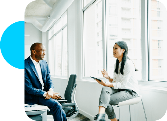 a man sitting on a table looking at a woman talking holding an ipad with a blue circle in the corner