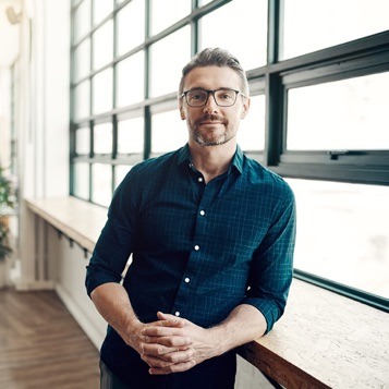 man leaning against a counter next to a window looking at the camera
