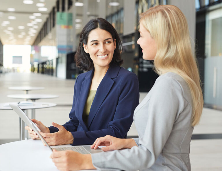 Two professional women talking over laptop in office space