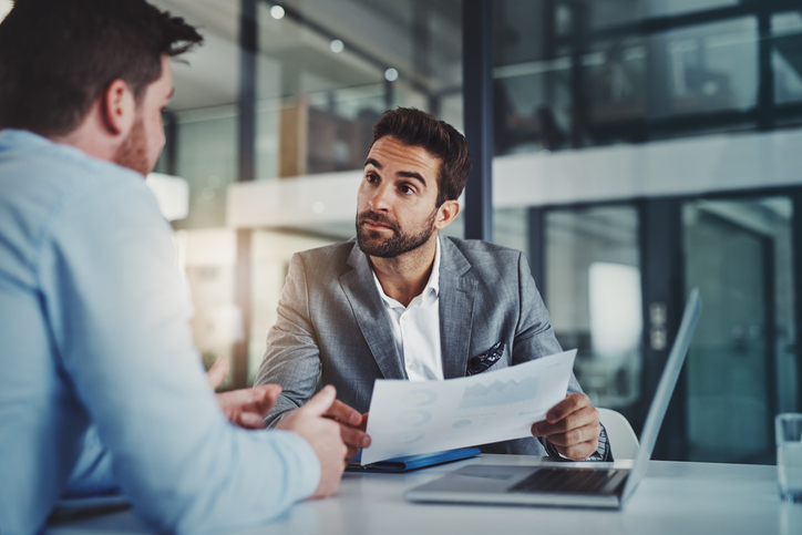 two men discussing over piece of paper while one listens intently