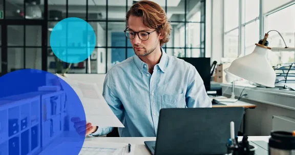 Young professional man reviewing paperwork at desk with laptop.